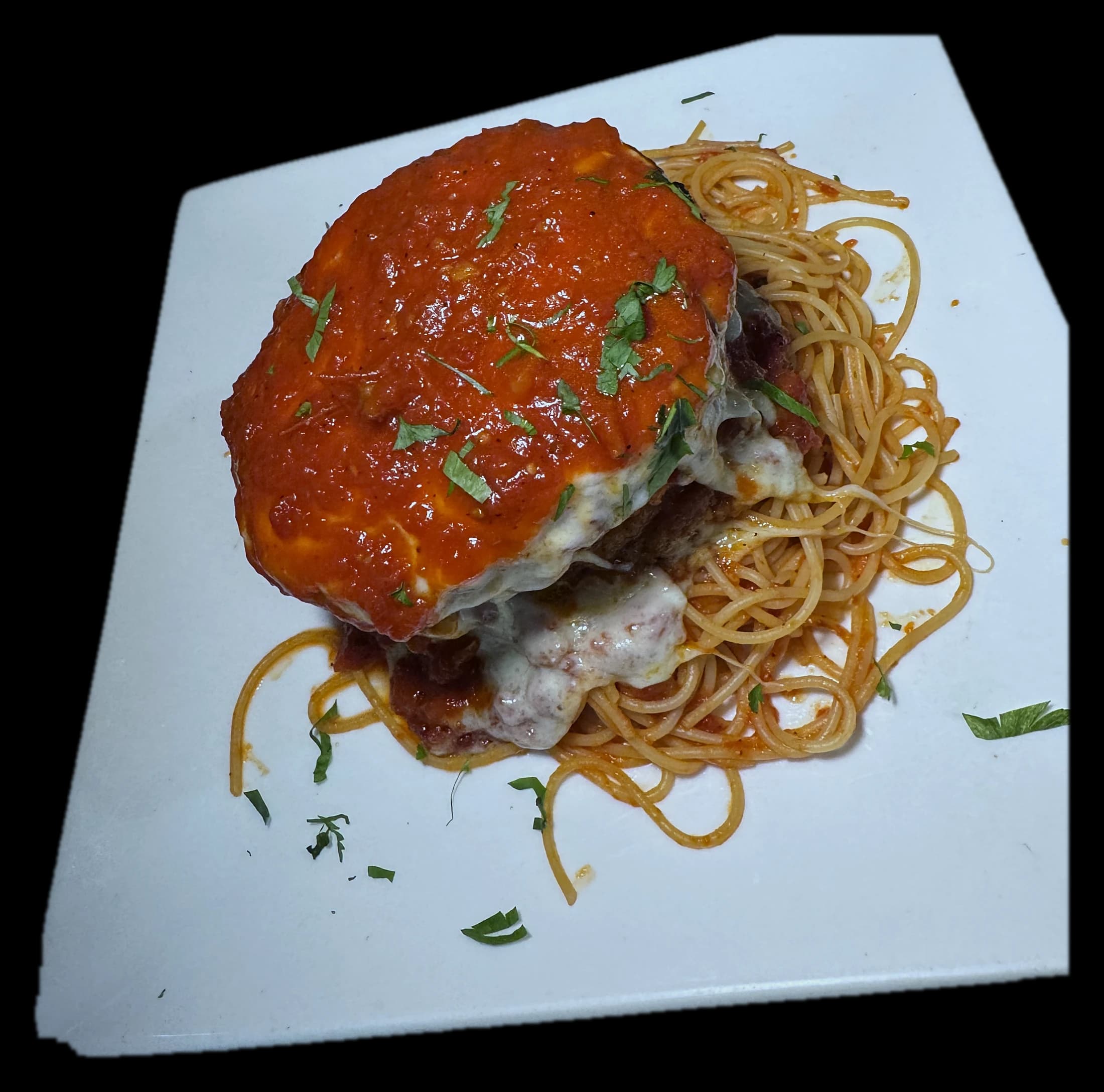 Eggplant parmigiana stacked tall under red sauce and melted mozzarella, over spaghetti
